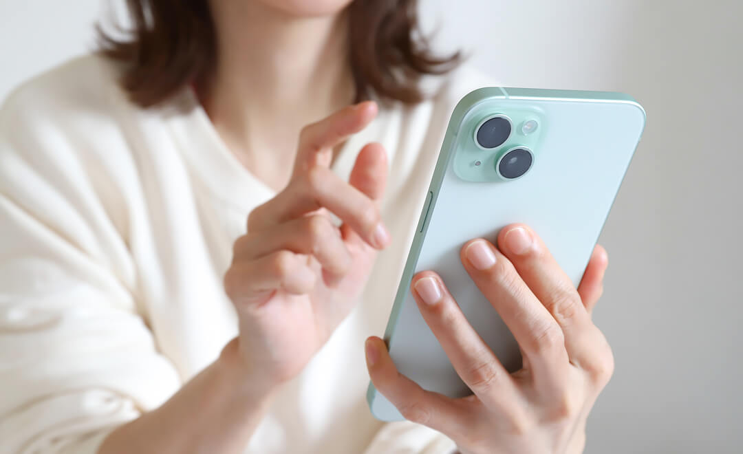 白い服を着た女性が、スマートフォンを片手に持ち、もう一方の手で画面を操作している様子