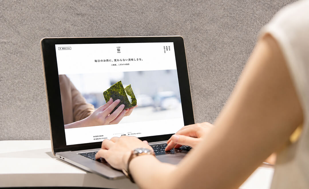 ノートパソコンに表示されたウェブサイトを見ながら、キーボード操作し、デザイン制作をしている人物の様子